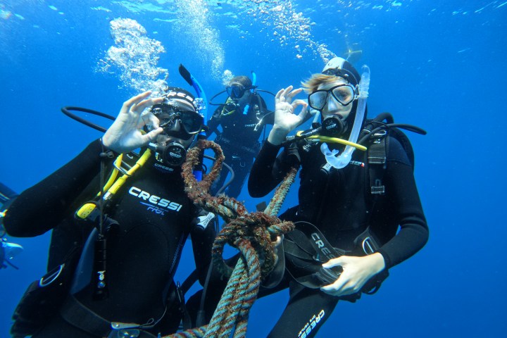 Two scuba divers underwater making OK hand signs near a rope.