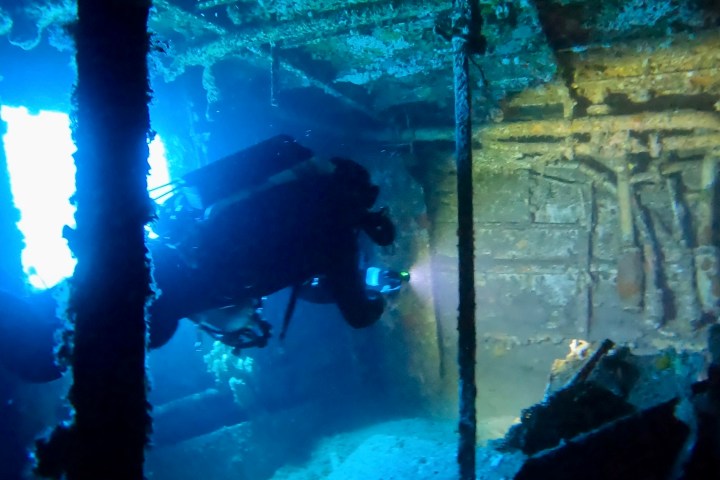 Scuba diver explores inside a shipwreck with beams of light streaming through.