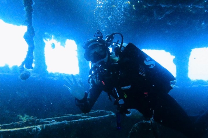 Scuba diver explores underwater shipwreck with visible light from above.