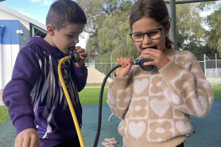 Two children using a hookah under a tent outdoors.
