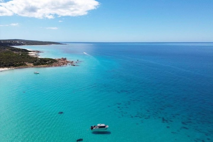 A boat on clear turquoise water near a coastline under a blue sky.