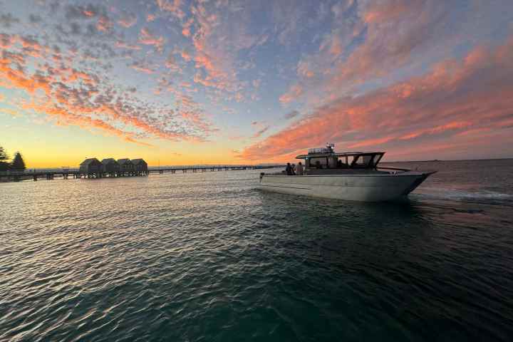 Boat on water near a pier with huts at sunset, colorful sky.