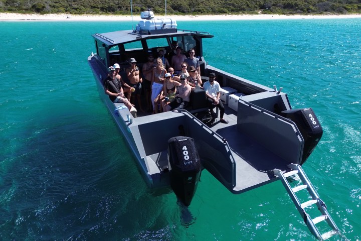 Group of people enjoying a ride on a motorboat in blue water near a beach.